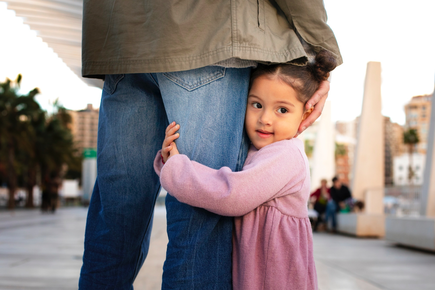 Una niña vestida de rosa abraza la pierna de un adulto que lleva vaqueros azules.
