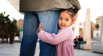 Una niña vestida de rosa abraza la pierna de un adulto que lleva vaqueros azules.