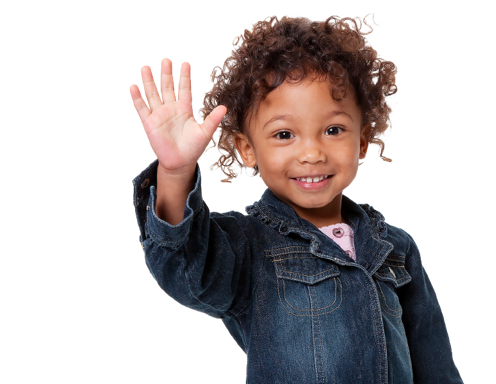 Una niña pequeña de tez marrón y pelo oscuro enrulado, vistiendo una chaqueta de denim y sonriéndo a la cámara con su mano alzada y saludando.