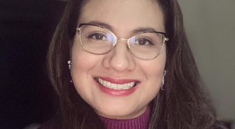 Adriana Morales Lemus, con suéter morado y gafas, sonríe a la cámara.