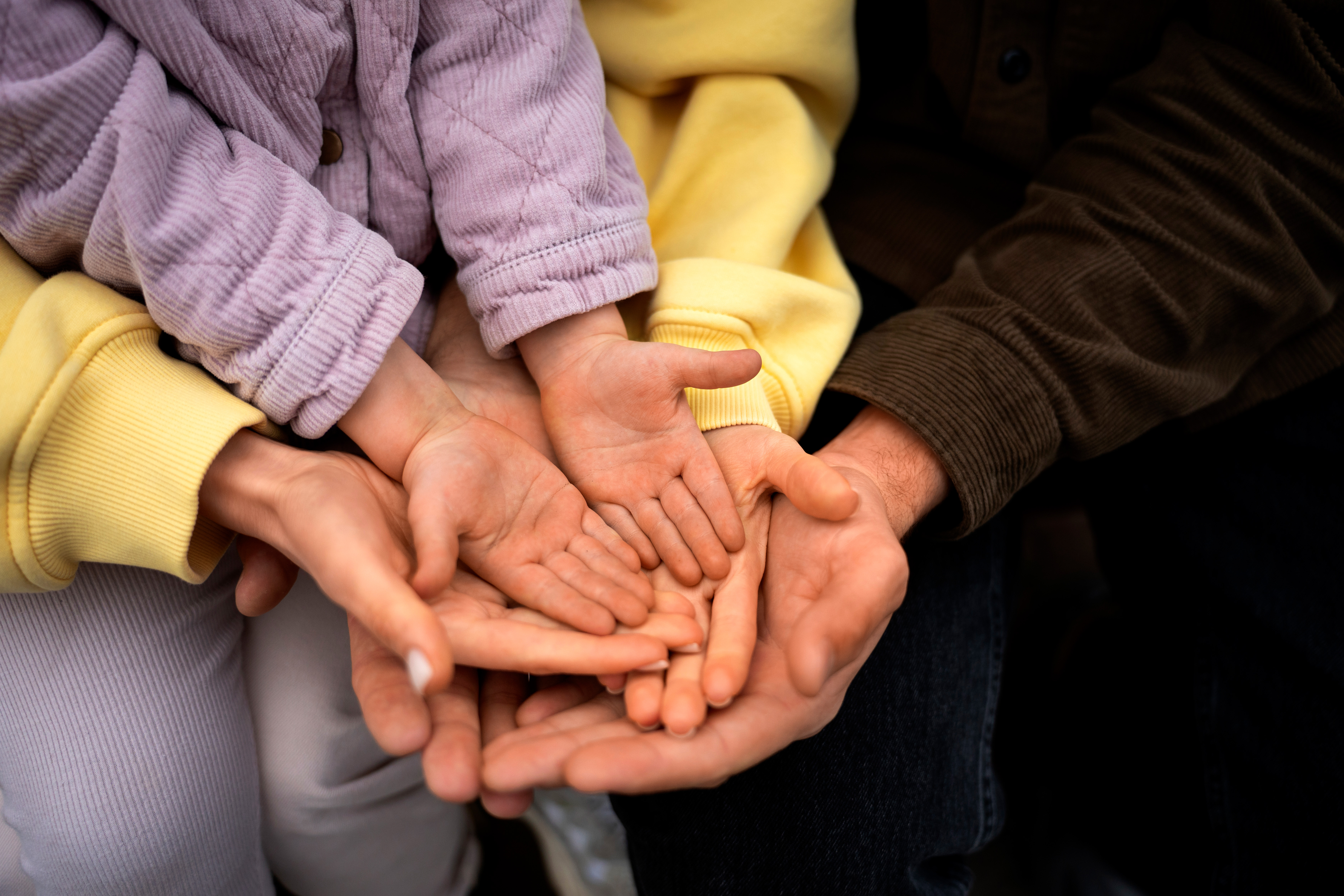 Dos manos de figuras paternas sosteniendo la mano de un niño pequeño