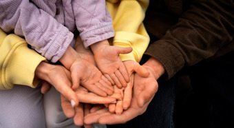 Dos manos de figuras paternas sosteniendo la mano de un niño pequeño