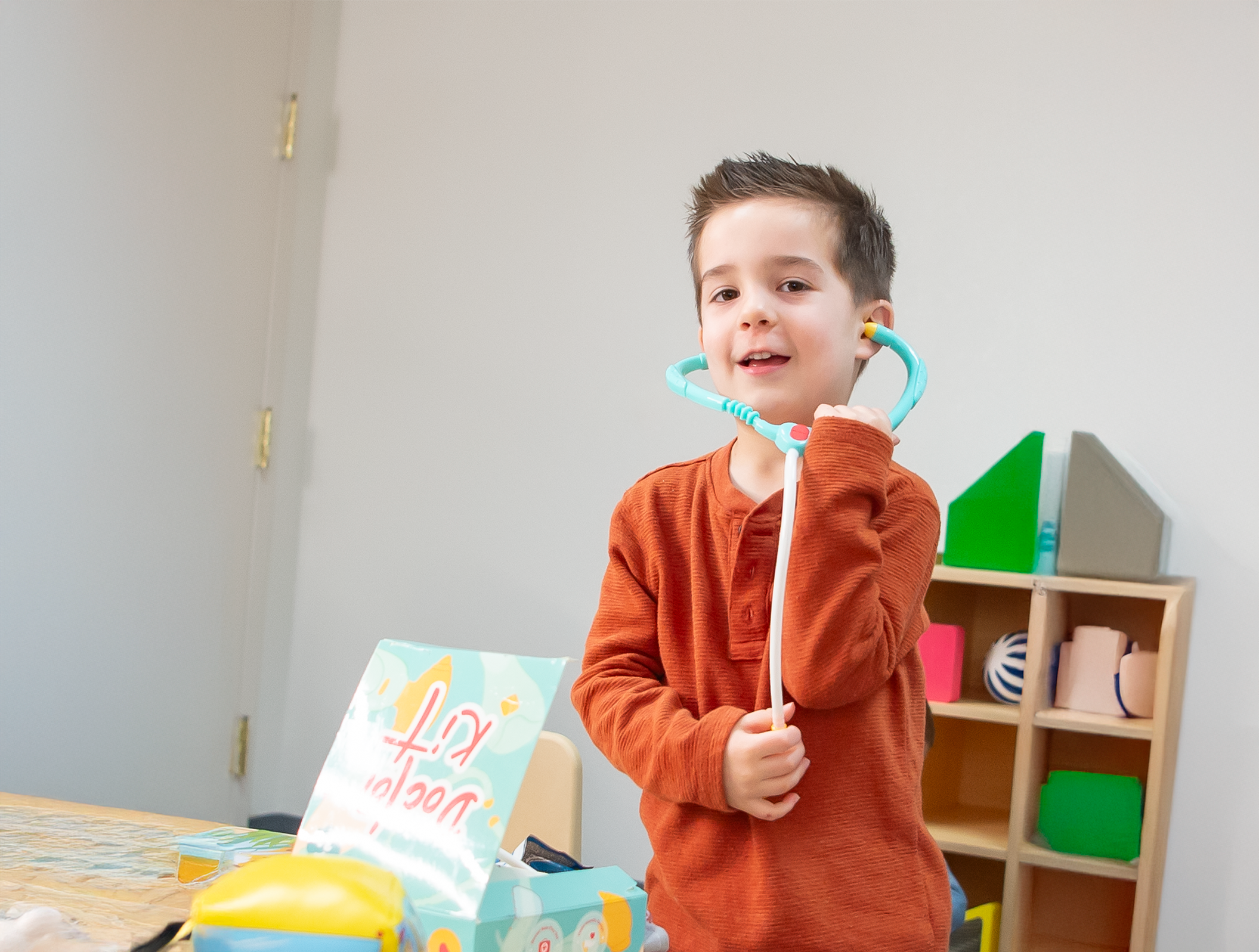 Un niño con una camisa naranja juega con un estetoscopio de juguete