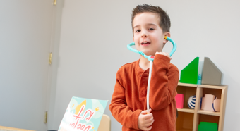 Un niño con una camisa naranja juega con un estetoscopio de juguete