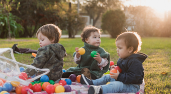 Tres niños pequeños sentados afuera en el césped, jugando con juguetes de colores del arco iris.