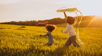 Dos niños pequeños jugando con cometas, mientras corren por un campo de hierba durante la puesta del sol.
