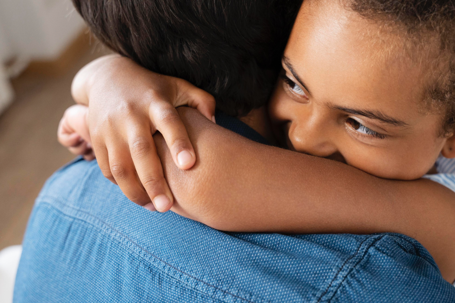 Primer plano de un niño abrazando a un adulto, con camisa vaquera. El niño sonríe.