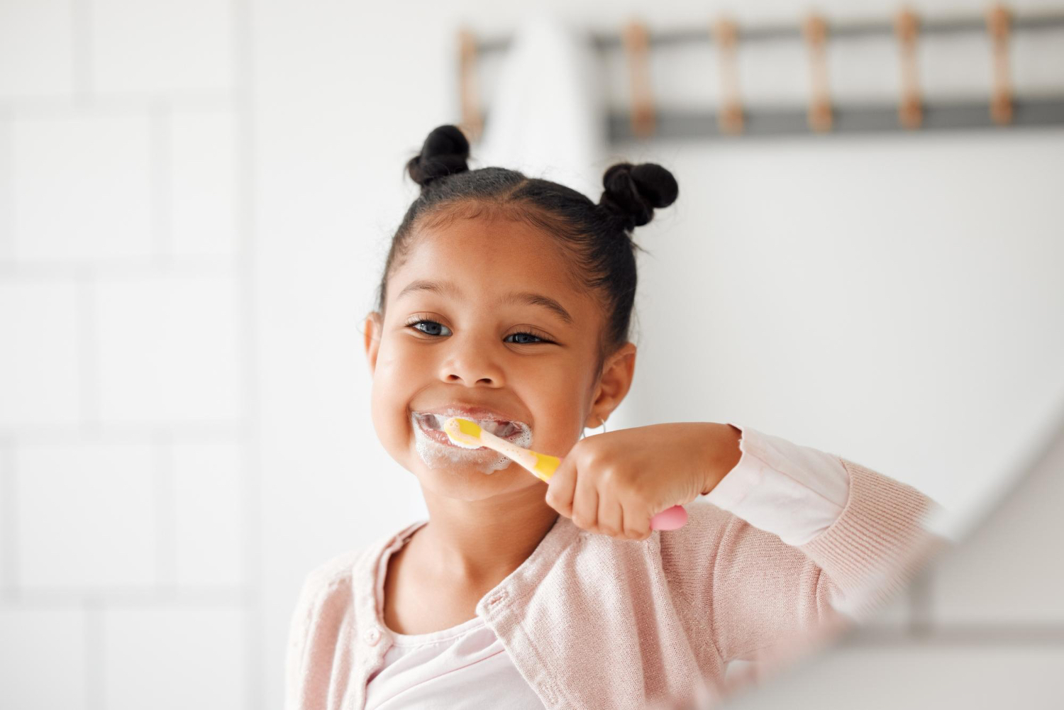 Una niña pequeña con una camiseta rosa se está cepillando los dientes con pasta de dientes, que tiene esparcida por toda la cara.
