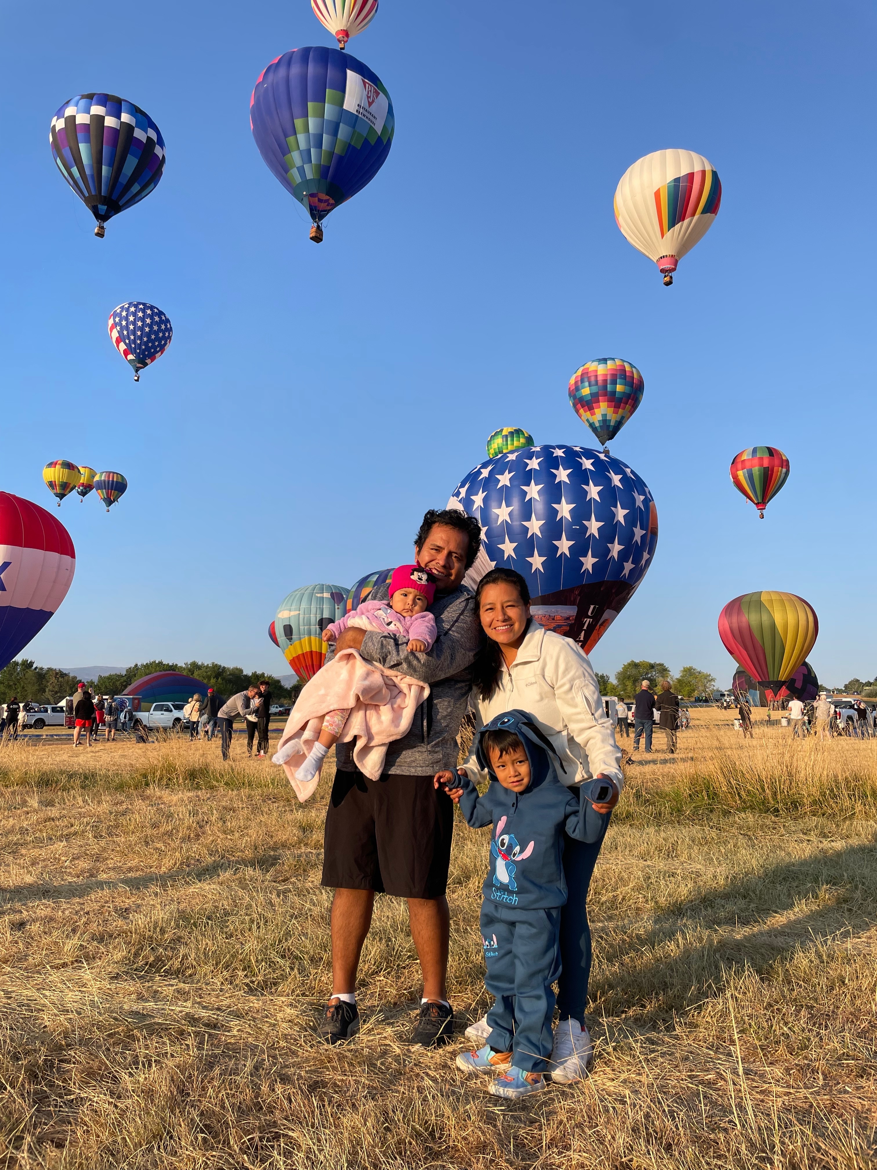 Angela Oscanoa con su familia en un campo de globos aerostáticos. Varios globos aerostáticos flotan detrás de ellos.