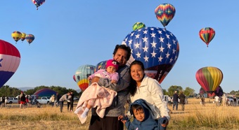 Angela Oscanoa con su familia en un campo de globos aerostáticos. Varios globos aerostáticos flotan detrás de ellos.