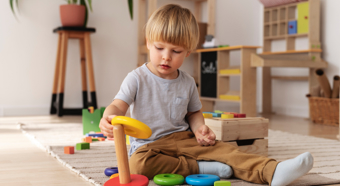 Un niño pequeño se sienta en el suelo y juega con juguetes de bloques de colores.