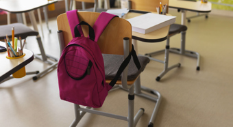 Interior de un aula con una mochila rosa en el respaldo de la silla del escritorio de la escuela.