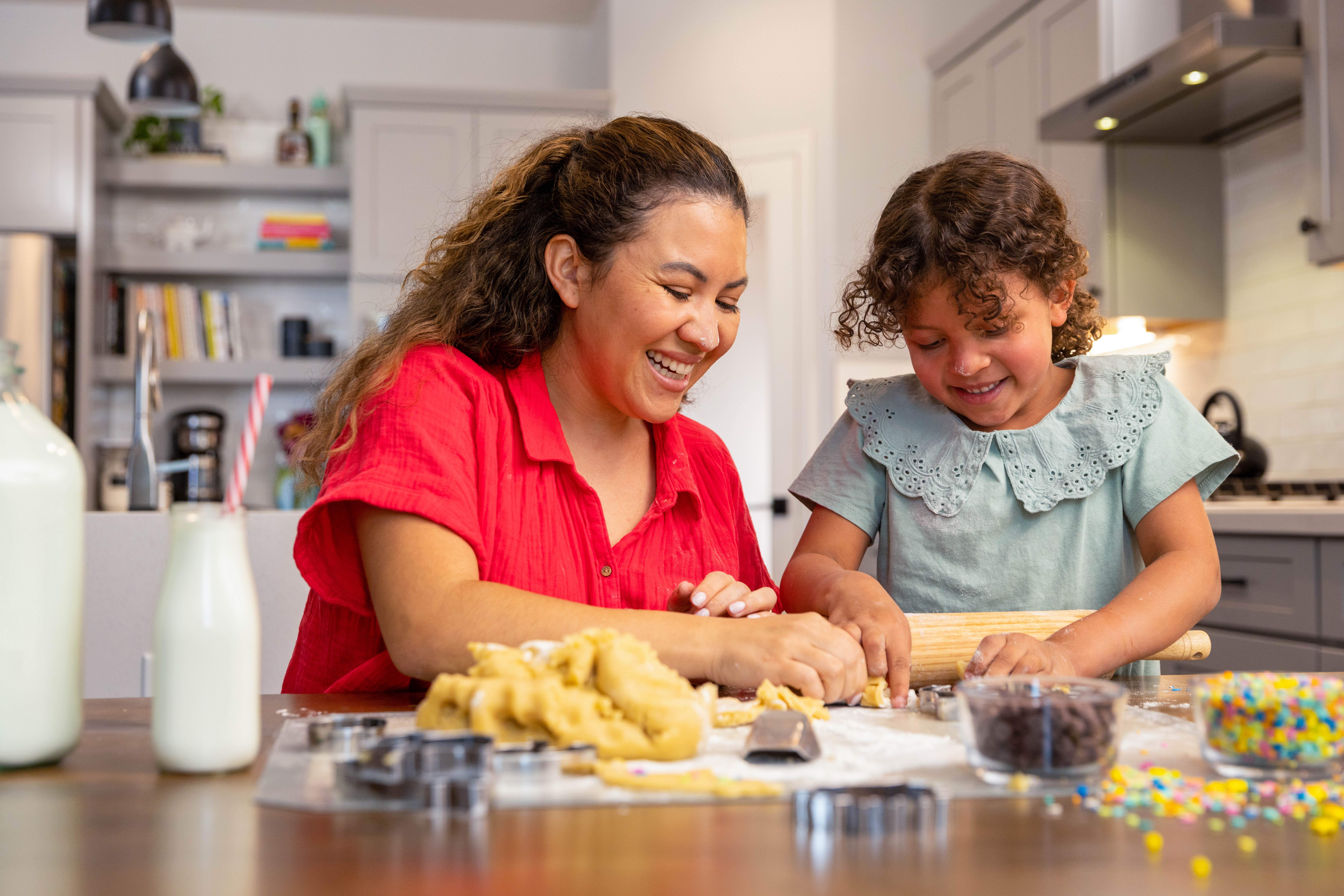 Una niña pequeña y una mujer adulta están sentadas en la cocina riendo y preparando galletas de azúcar navideñas.