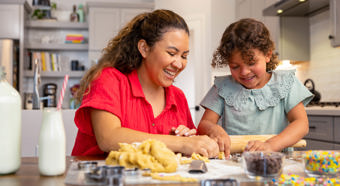Una niña pequeña y una mujer adulta están sentadas en la cocina riendo y preparando galletas de azúcar navideñas.