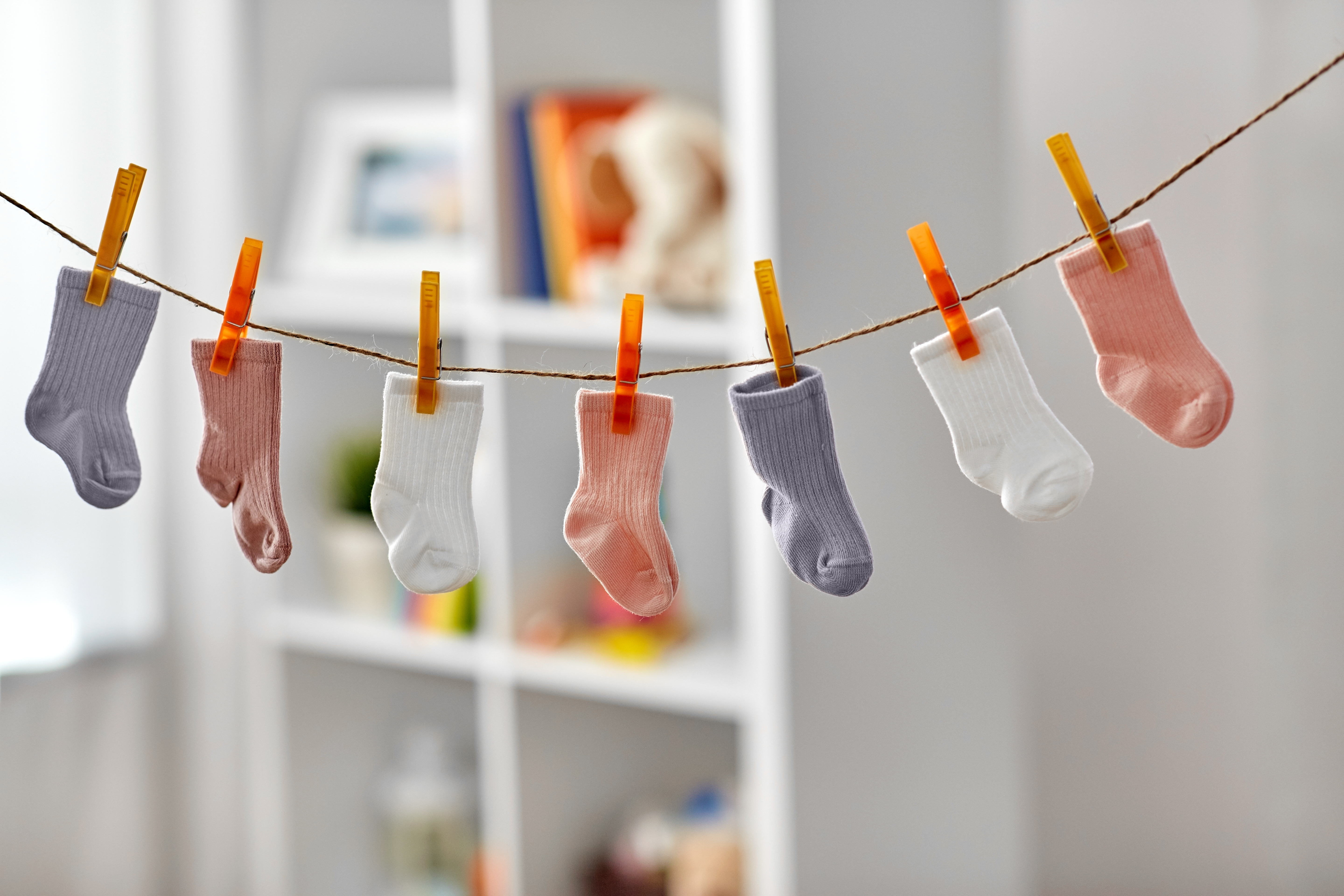 7 calcetines de colores para niños pequeños colgados en un tendedero en el interior.