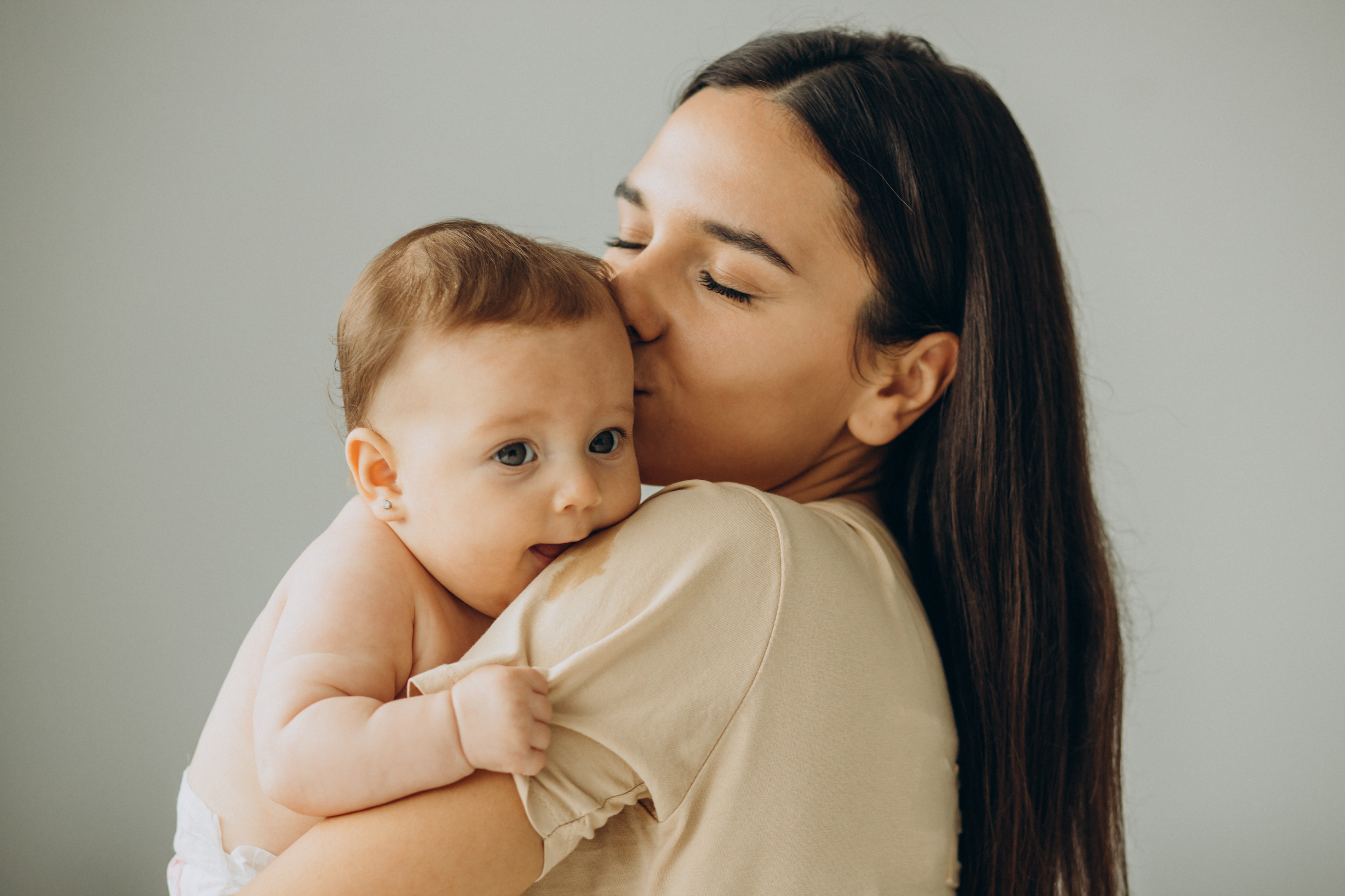 Mujeres de cabello castaño sosteniendo y besando a un bebé sonriente en la cabeza