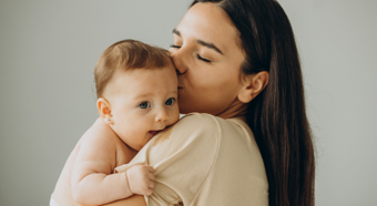 Mujeres de cabello castaño sosteniendo y besando a un bebé sonriente en la cabeza