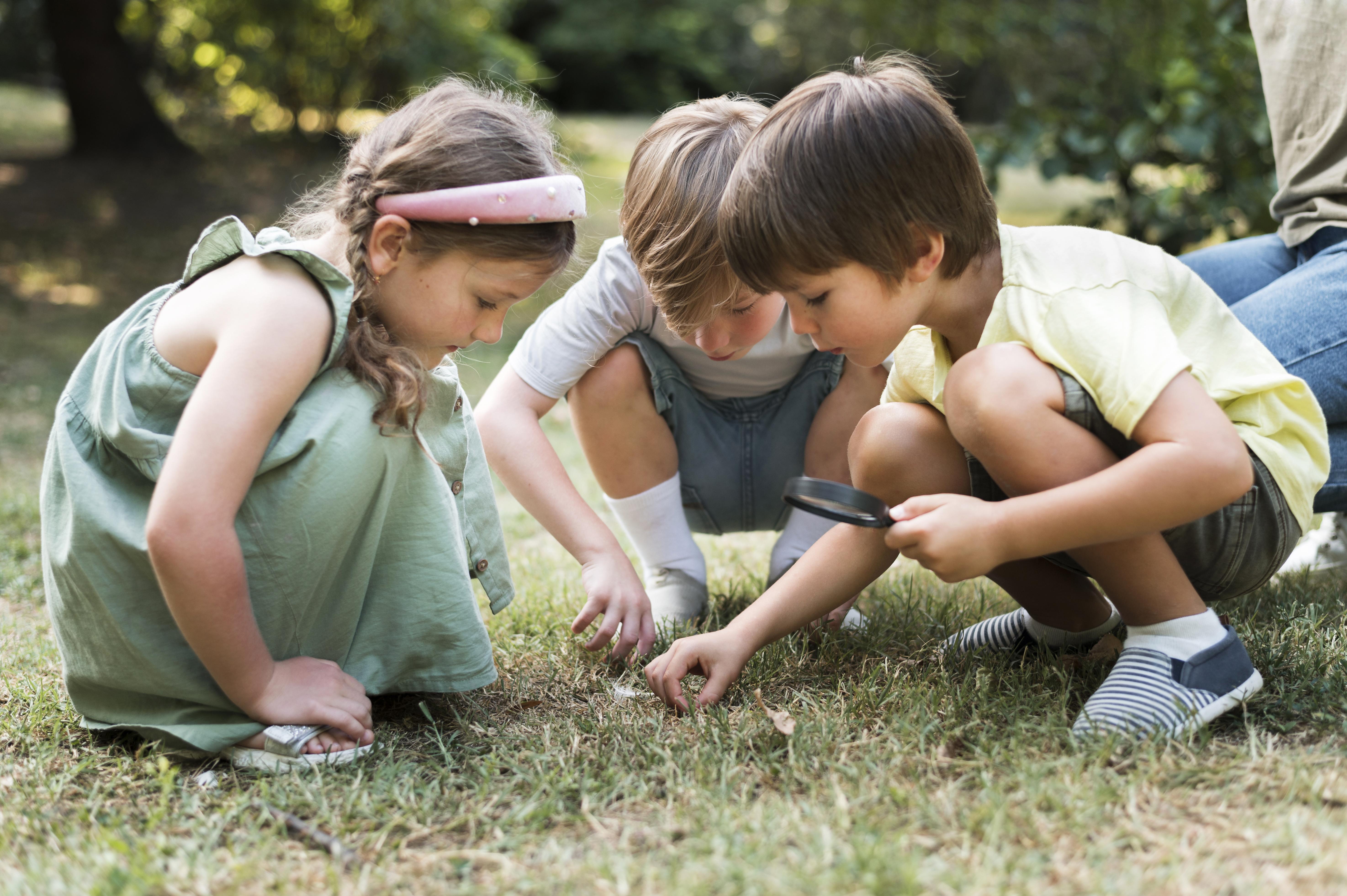 Tres niños pequeños buscando insectos en la hierba.