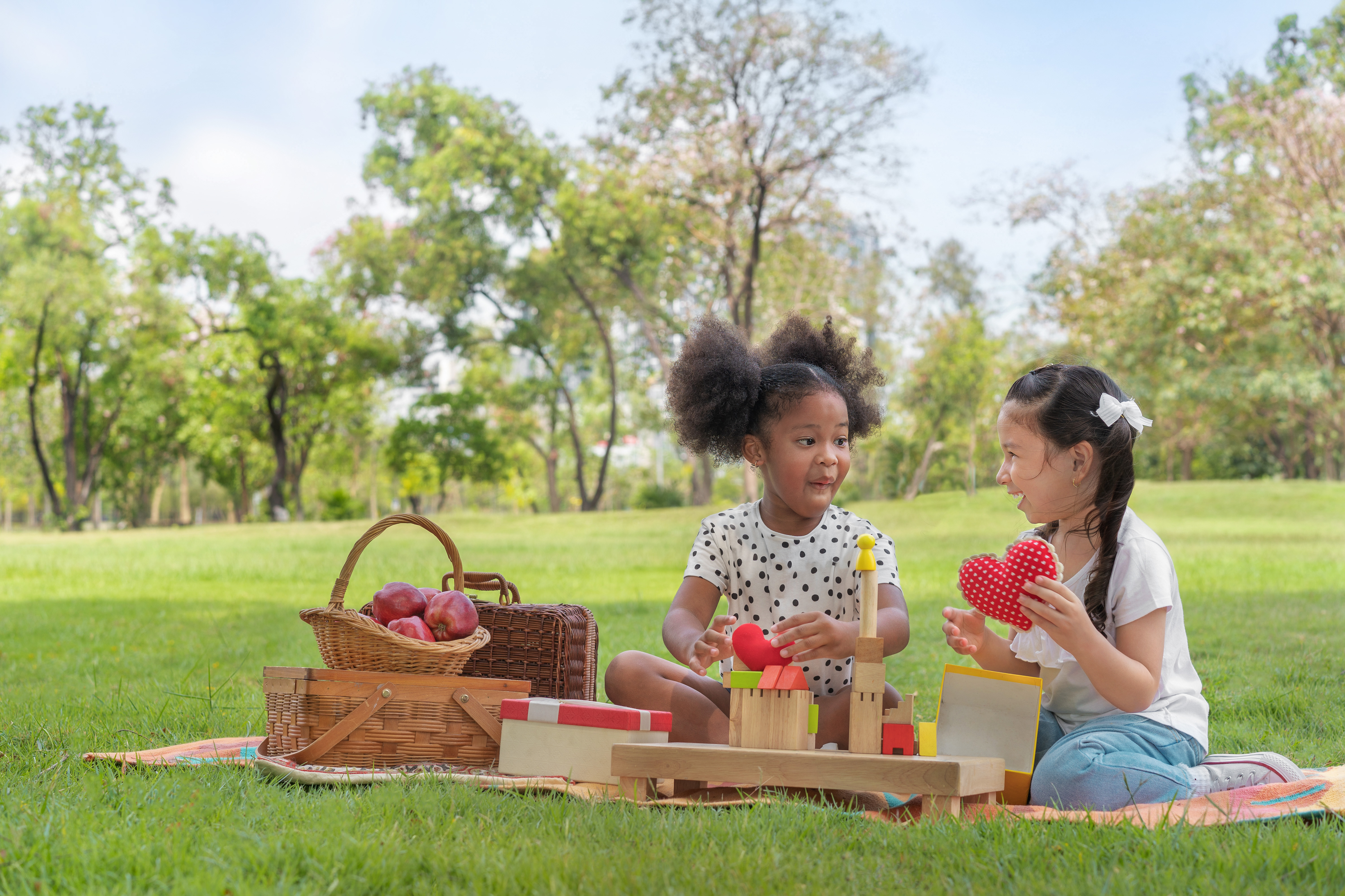 Dos chicas jóvenes haciendo un picnic en un parque sobre el césped verde, con una cesta de picnic con manzanas.