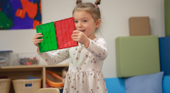 Niña jugando con juguetes rojos y verdes en un salón de clases