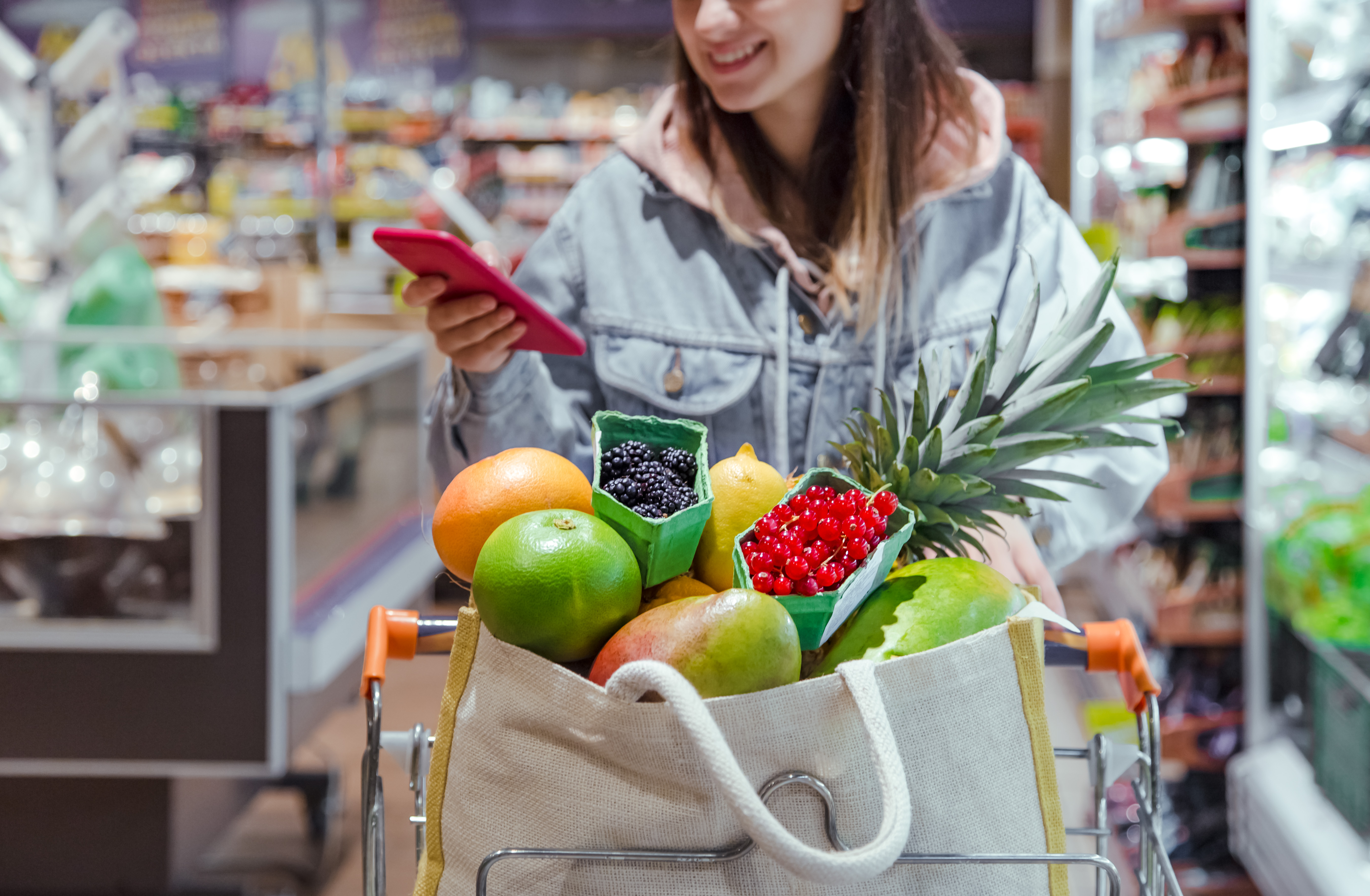 Mujeres jóvenes con un carrito de compras lleno de frutas y verduras, mirando su teléfono mientras sonríen