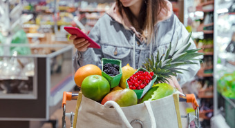 Mujeres jóvenes con un carrito de compras lleno de frutas y verduras, mirando su teléfono mientras sonríen