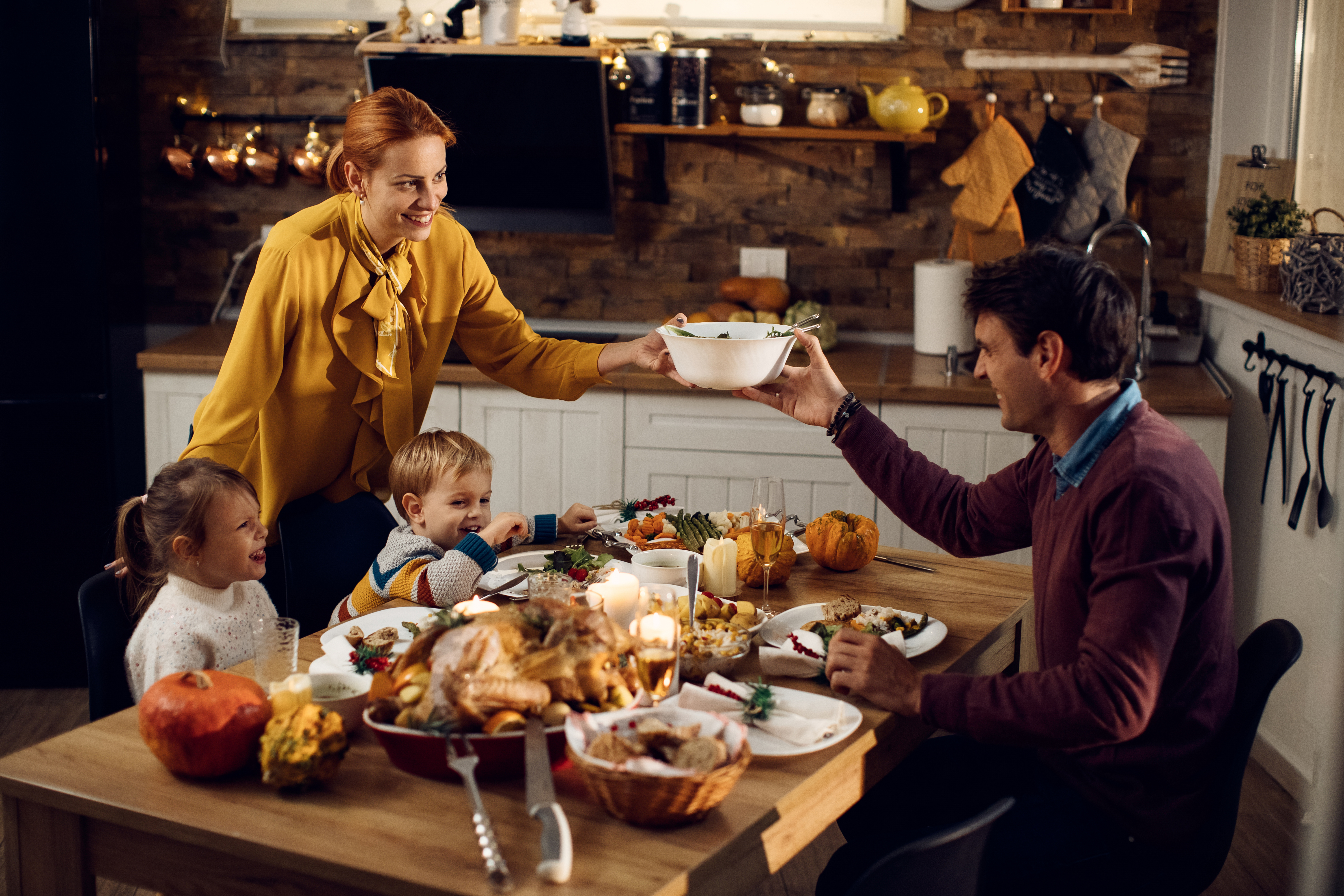 Mesa de cena de Acción de Gracias con alimentos de Acción de Gracias cubriendo la mesa, un niño, una niña y dos adultos sentados alrededor de la mesa riendo y sonriendo