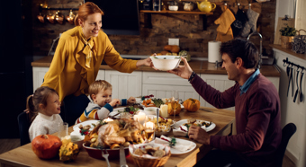 Mesa de cena de Acción de Gracias con alimentos de Acción de Gracias cubriendo la mesa, un niño, una niña y dos adultos sentados alrededor de la mesa riendo y sonriendo