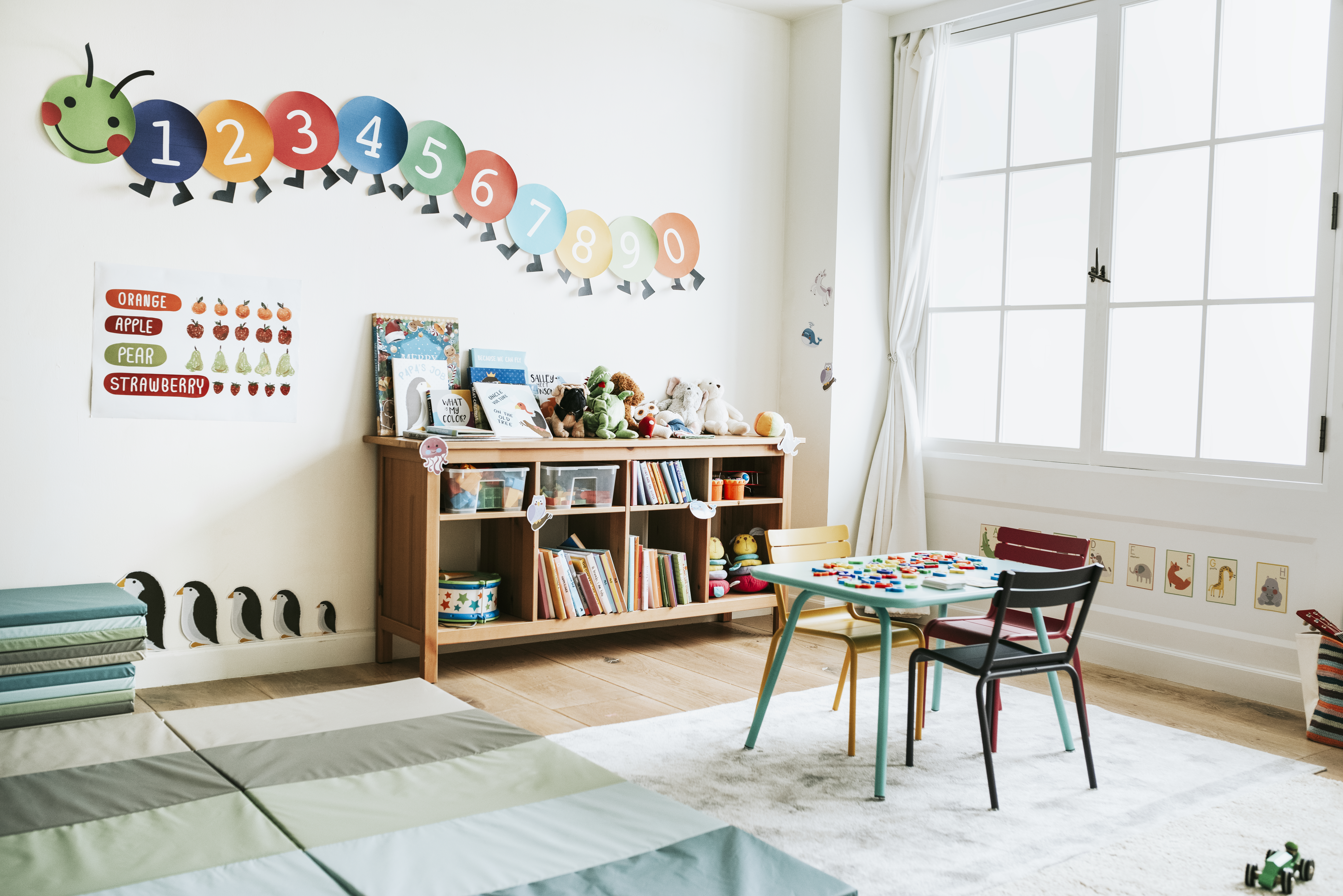 Interior de un aula de preescolar con estanterías, un pequeño escritorio y divertidos gráficos educativos en las paredes.