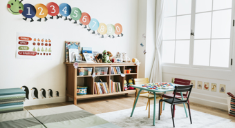 Interior de un aula de preescolar con estanterías, un pequeño escritorio y divertidos gráficos educativos en las paredes.