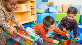 Tres niños pequeños sentados en el suelo jugando con bloques de juguete coloridos.