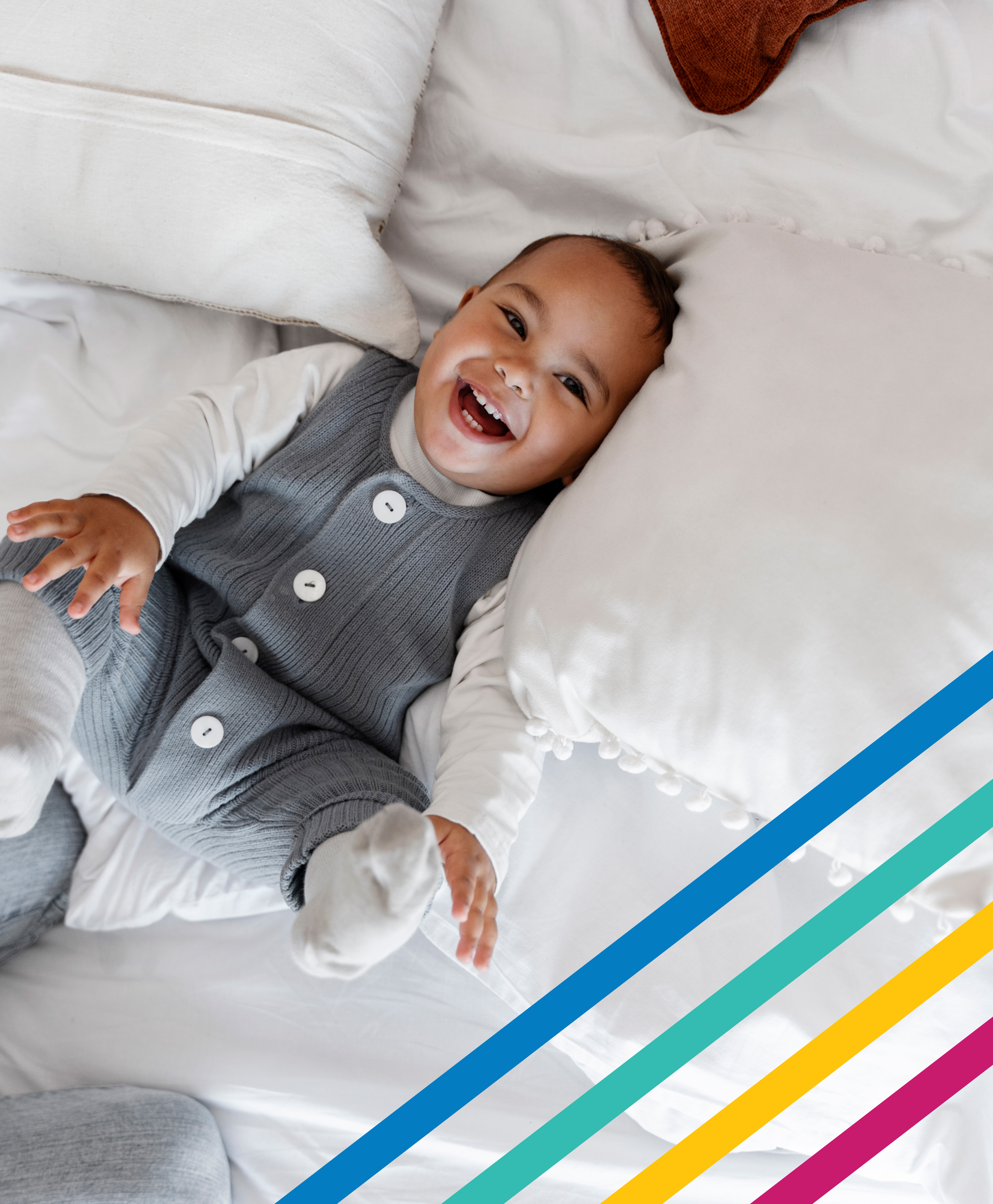 Un bebé está acostado en una cama completamente blanca, riendo y sonriendo.