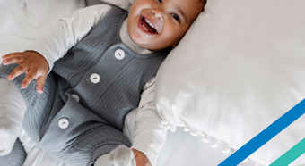 Un bebé está acostado en una cama completamente blanca, riendo y sonriendo.