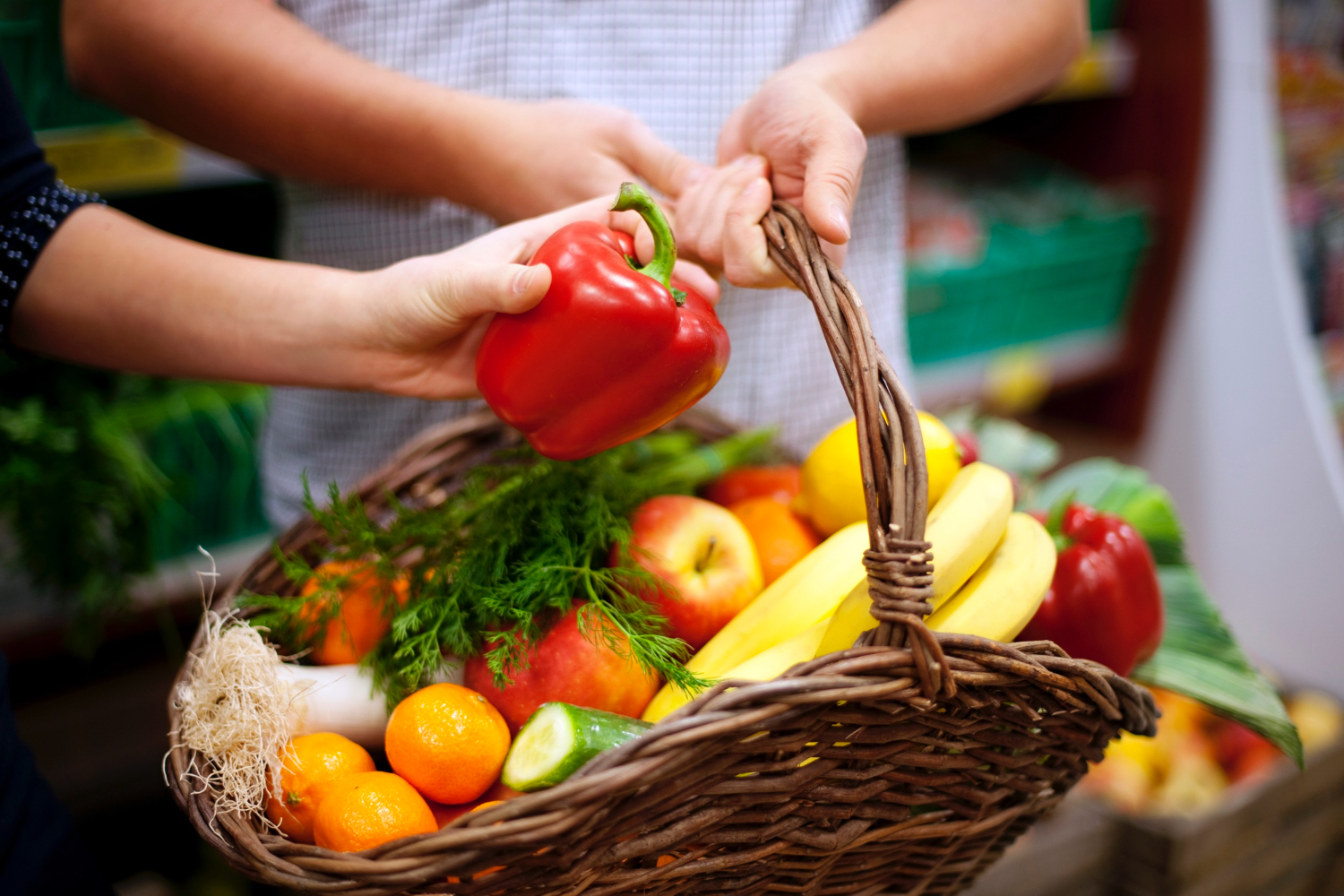 Primer plano de una mano que introduce la mano en una cesta llena de diversas frutas y verduras.