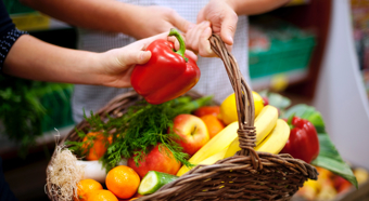 Primer plano de una mano que introduce la mano en una cesta llena de diversas frutas y verduras.