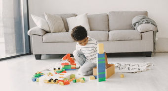 Un niño pequeño está sentado en medio de la sala de estar, jugando con varios juguetes y bloques.