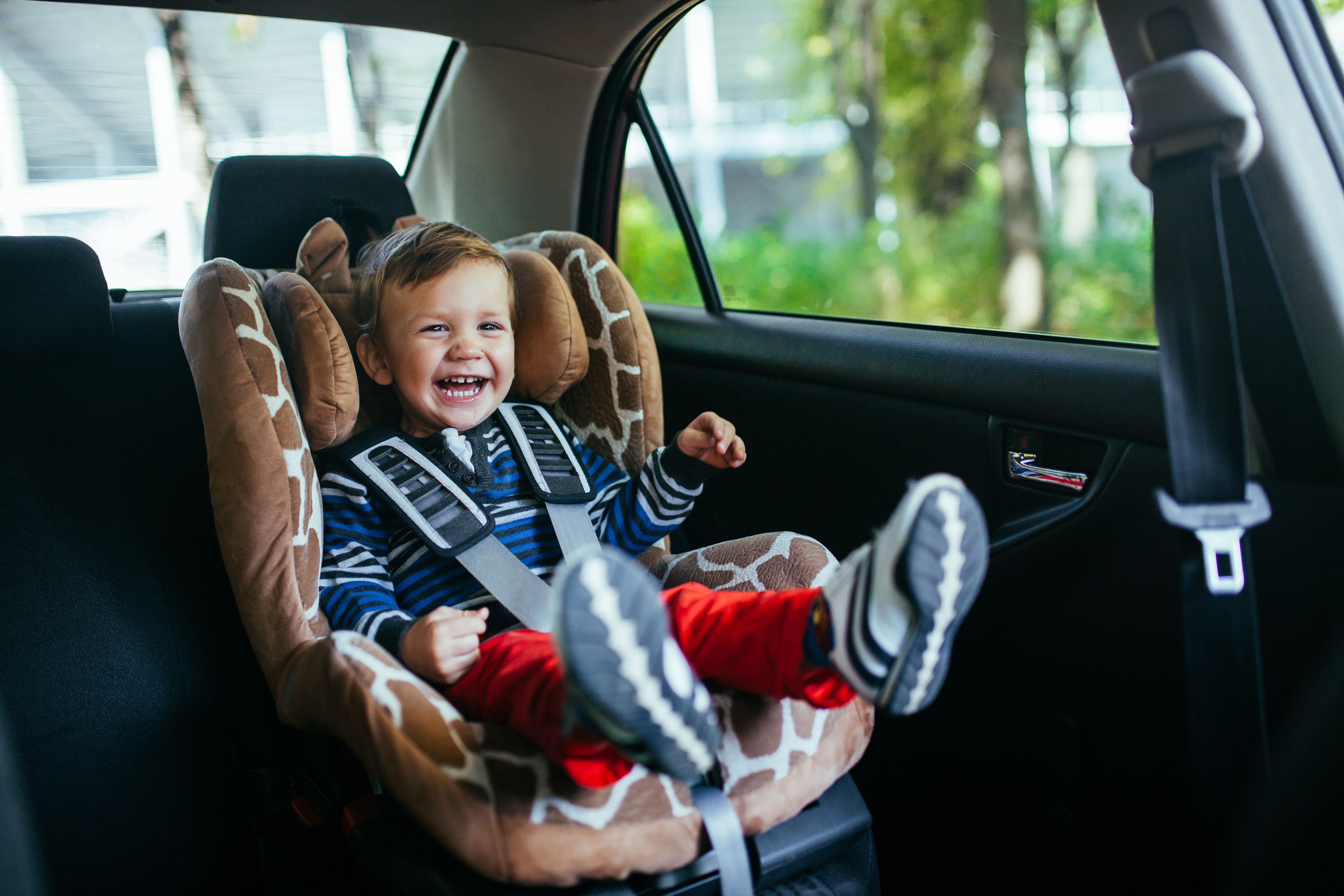 Adorable y sonriente niño sentado en un asiento de seguridad para el automóvil