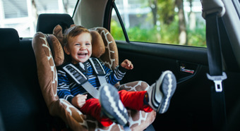 Adorable y sonriente niño sentado en un asiento de seguridad para el automóvil