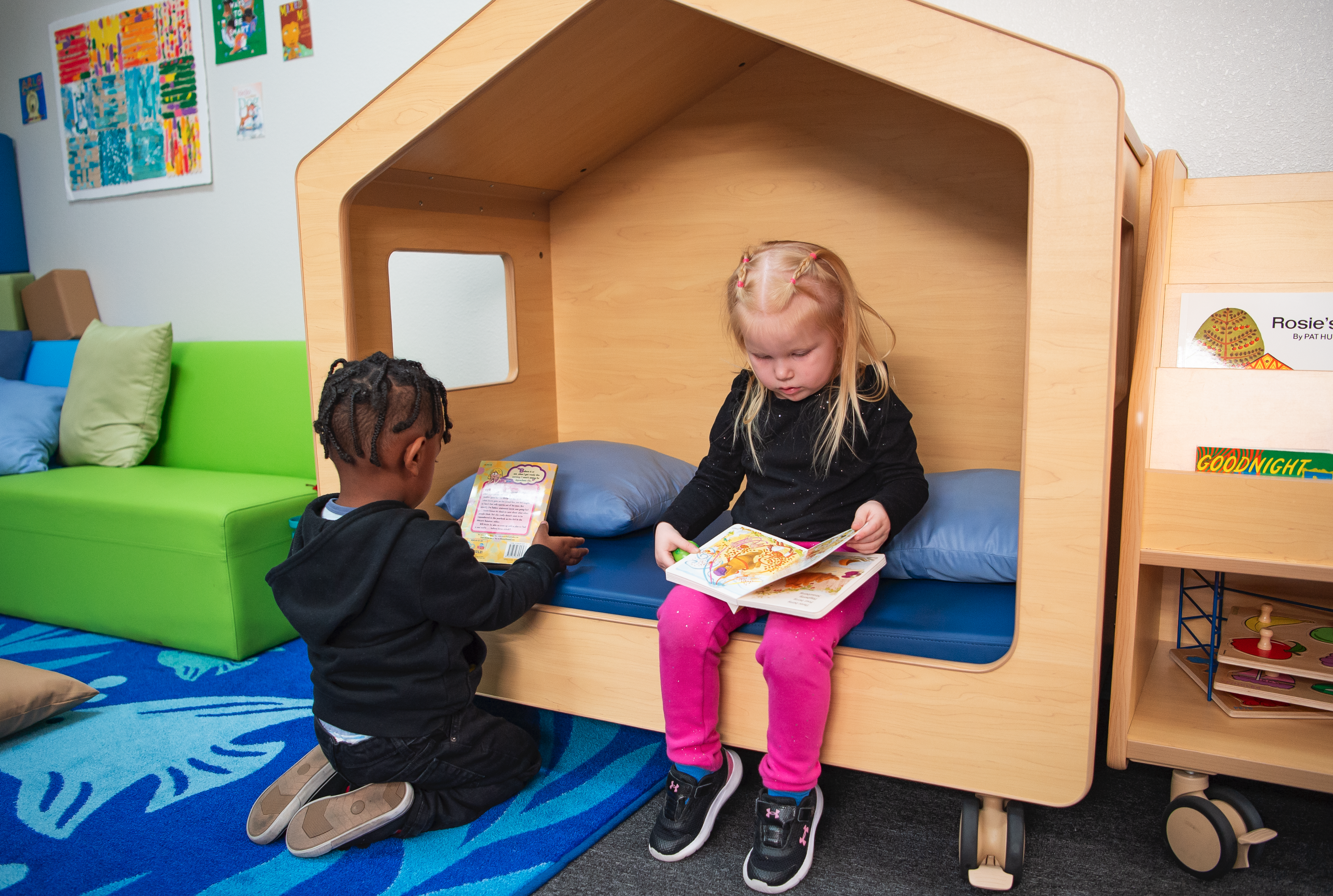 Dos niños pequeños sentados uno al lado del otro mientras leen libros infantiles en una casa de juegos para niños.