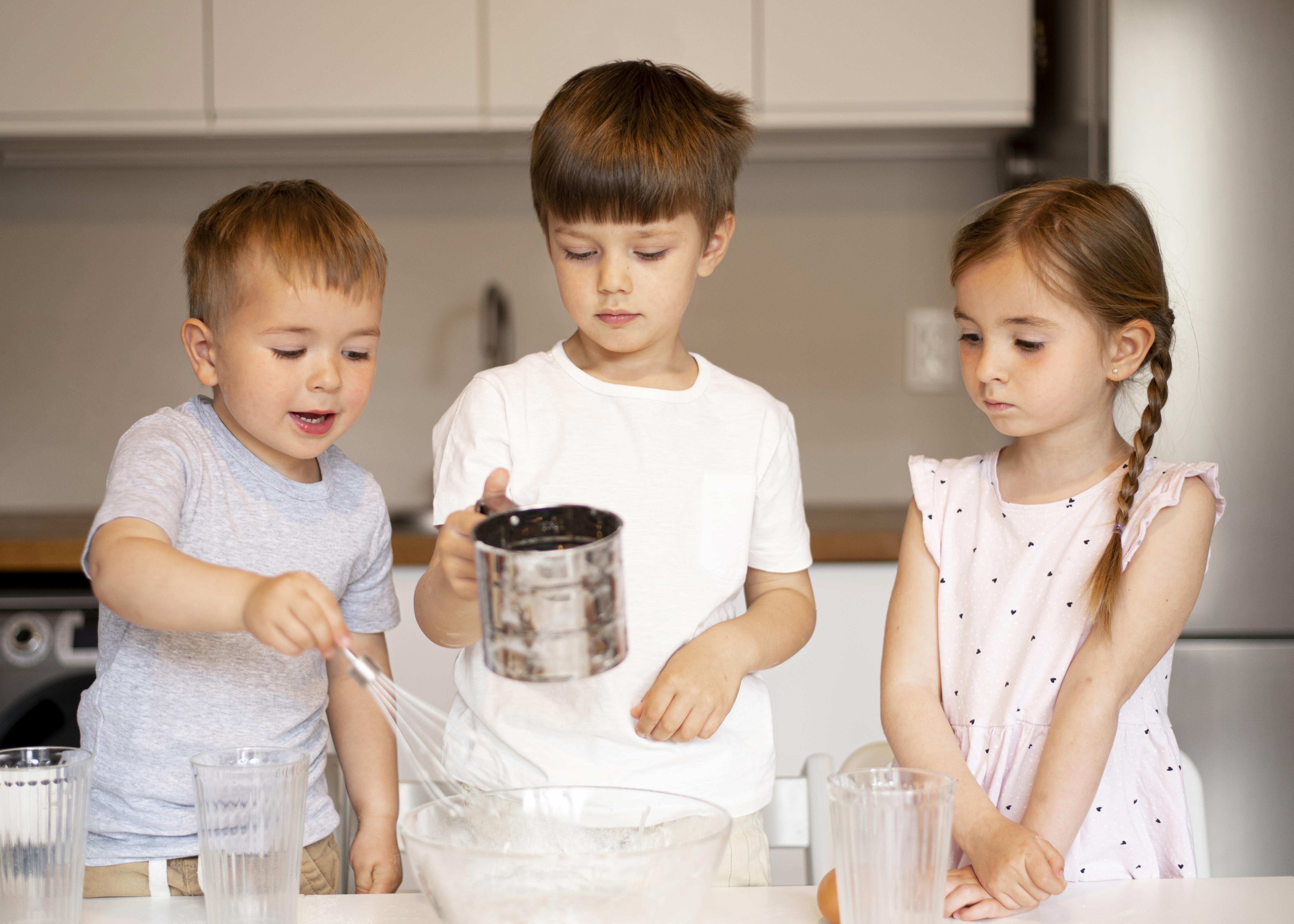 Tres niños pequeños en la cocina de una casa ayudando con algo de cocina básica.
