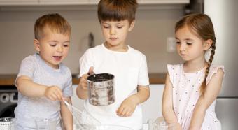 Tres niños pequeños en la cocina de una casa ayudando con algo de cocina básica.
