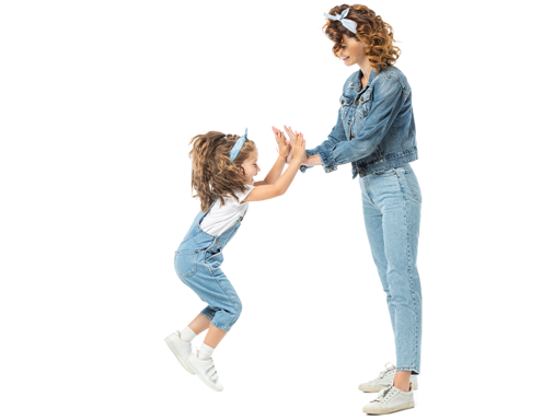 Una mujer de piel clara chocando ambas manos con una niña que está saltando en el aire, ambas vestidas con conjuntos de denim.