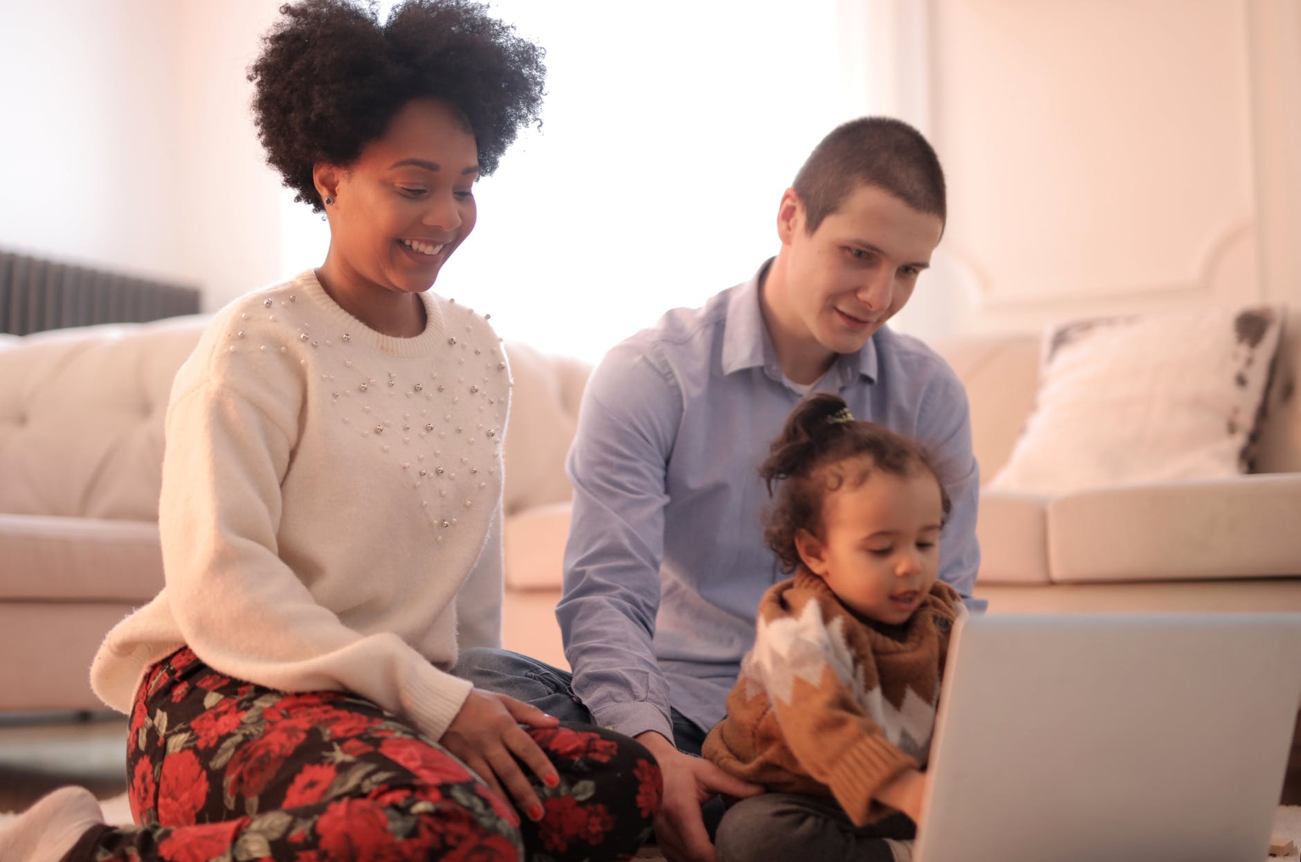 Una mujer y un hombre jóvenes se sientan con un niño pequeño en el suelo, mientras todos miran la pantalla de una computadora portátil. Un ambiente acogedor en el interior.
