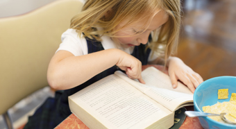 Una niña de cabello rubio apuntando con el dedo a un libro, preparándose para el primer día de clases.