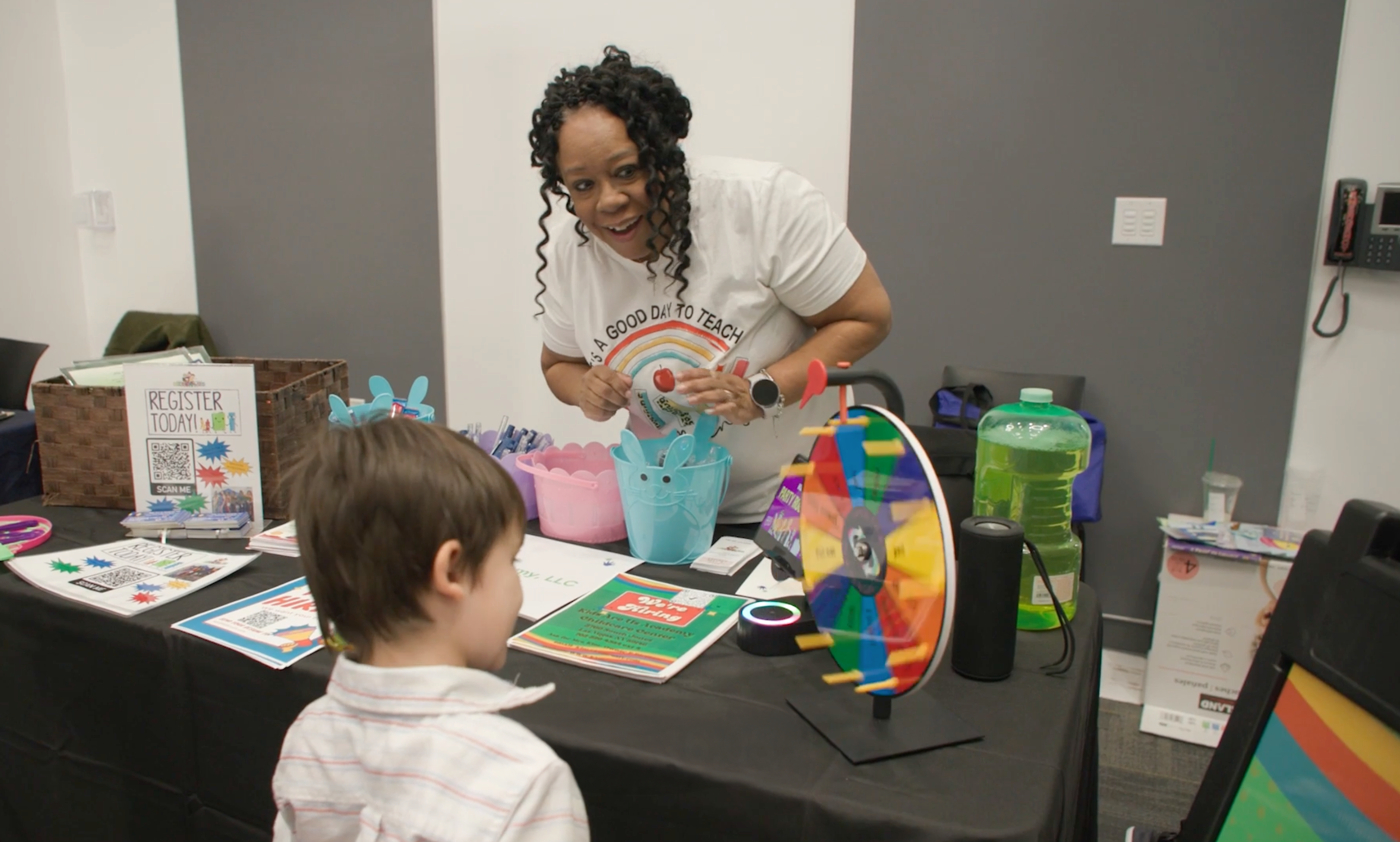 Un niño pequeño de cabello castaño juega con una rueca en un evento comunitario.