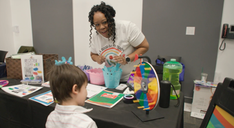 Un niño pequeño de cabello castaño juega con una rueca en un evento comunitario.