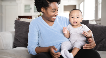 Alegres mujeres afroamericanas sonríen a su bebé en su regazo mientras están sentadas en el sofá.