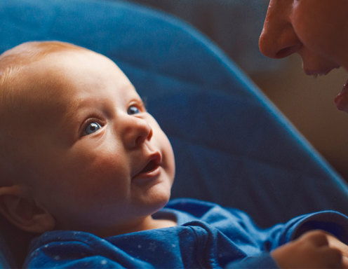 Un niño de tez clara y ojos azules, mirando hacia la cara fuera de cuadro de una mujer adulta sonriente.