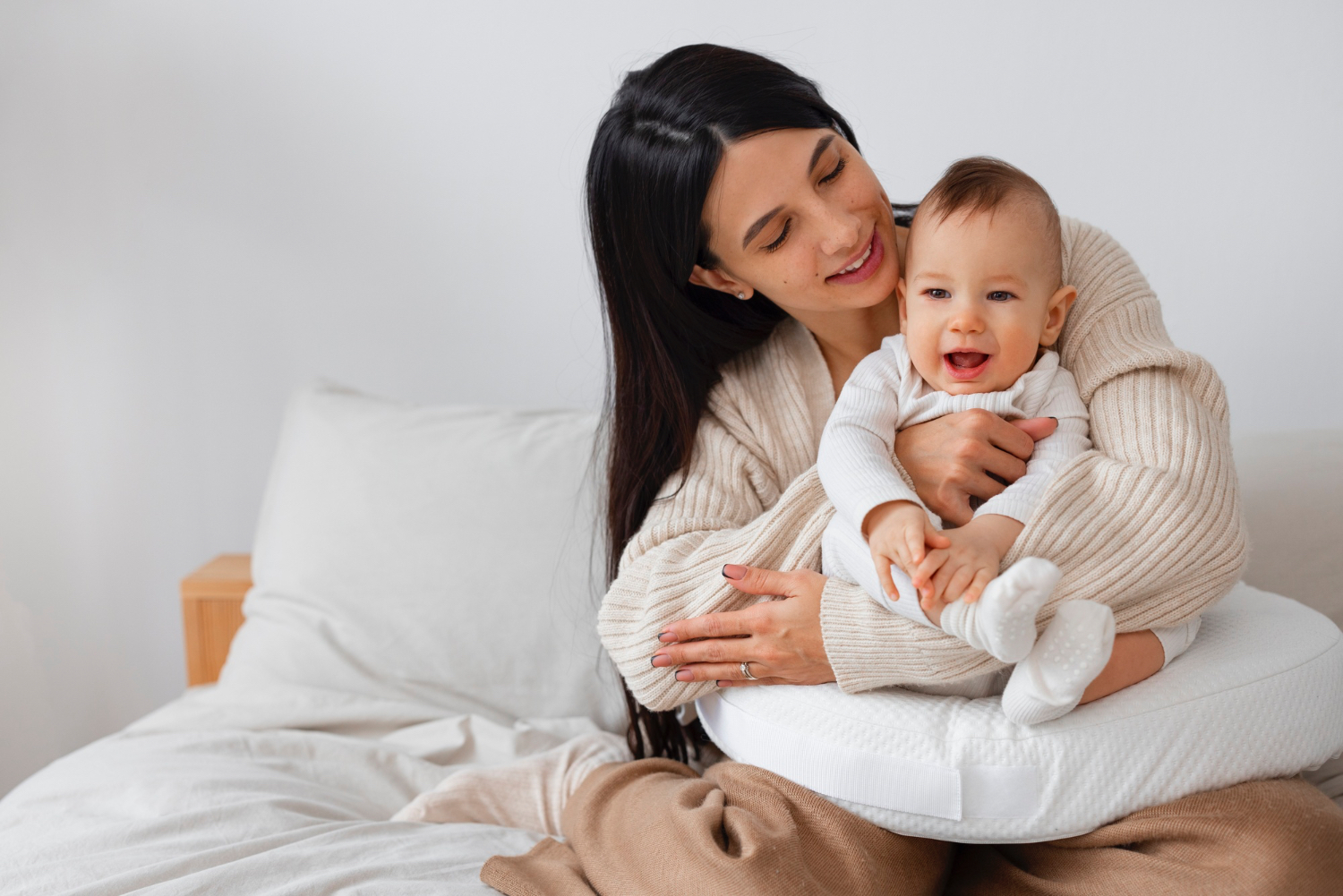 Mujeres sosteniendo a un bebé recién nacido en una cama completamente blanca, ambas sonriendo