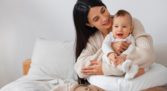Mujeres sosteniendo a un bebé recién nacido en una cama completamente blanca, ambas sonriendo